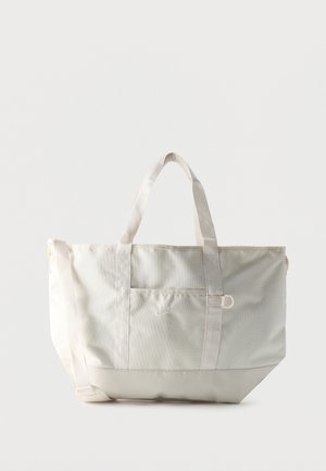 Sac cabas blanc Nike avec deux poignées, une poche avant et une bandoulière réglable sur un fond uni.