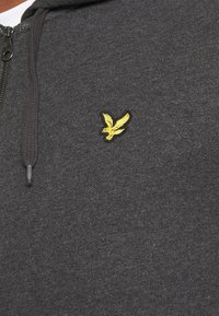 Felpa con zip grigia scura, dotata di un piccolo logo di un uccellino giallo ricamato sul lato sinistro del petto e concordati cordini.