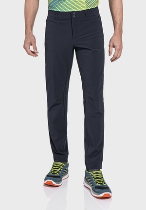 Marineblaue synthetische Hose mit einer taillierten Passform, ausgestattet mit zwei vorderen Knöpfen und Taschen, kombiniert mit mehrfarbigen Sportschuhen.