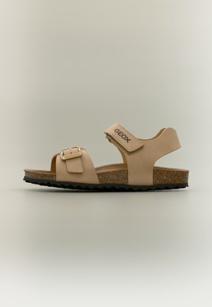 Sandalo beige aperto davanti con suola in sughero, cinturino regolabile con fibbia sul davanti e cinturino in velcro alla caviglia con il marchio "GEOX" su sfondo neutro.