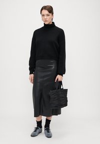 Suéter preto de malha com gola alta, combinado com uma saia midi de couro preta. Os acessórios incluem uma mala preta franzida e ténis cinzas.