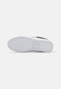 Shoe sole with patterned treads featuring repeated small logos and a circular larger logo near the heel on a white background.