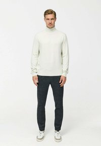 Pulover turtleneck gri deschis asociat cu pantaloni gri închis, având un design ajustat. Modelul poartă adidași albi cu accente gri.
