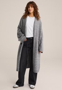 Pelēks garš kardigāns mīkstā diegu adījumā ar pārmērīgiem piedurknēm, priekšējām kabatām un ribotām piedurknēm, apvienots ar baltu blūzi un melniem platiem biksēm.