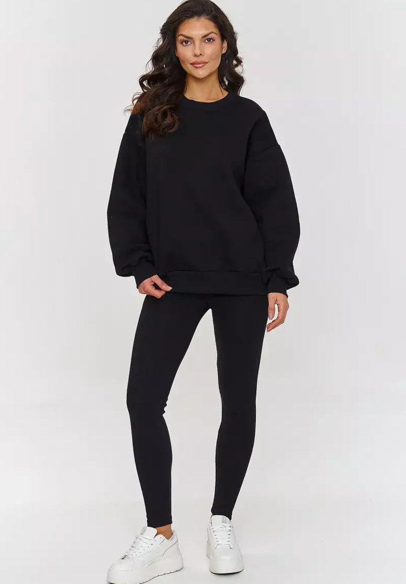 Czarny sweter z długimi rękawami, okrągłym dekoltem i luźnym krojem, zestawiony z czarnymi legginsami i białymi trampkami. Gładka faktura materiału.