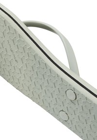 Lys grå flip-flop sål med et vinklet mønster, der har en sort kant og runde accenter. Glat tekstur med en fleksibel rem.