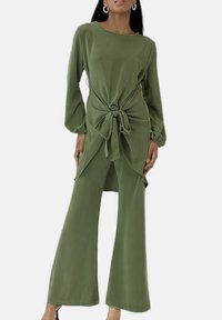 Olivgrünes Outfit mit einer gebundenen Taillendetail. Es verfügt über lange Ärmel, ein locker sitzendes Oberteil und ausgestellte Hosen. Glatter Stoff mit minimaler Textur.