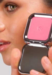 Kompakt rouge med rosa pulver i en firkantet panne, plassert i et metallisk sølvetui. Et speil er festet på innsiden av lokket.