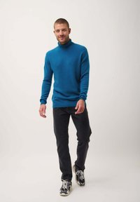 Maglione a collo alto turchese realizzato in materiale morbido, abbinato a jeans neri e sneakers con suola testurizzata e dettagli a contrasto.