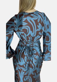 Robe en satin marron avec un motif floral bleu, à manches longues et un détail de taille noué. Texture lisse et silhouette fluide.
