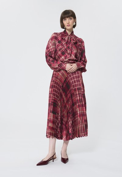 Rood geruite jurk met lange mouwen, strikkragen, geplooide rok en zwarte accenten; gecombineerd met bordeaux slingbackhakken.