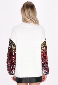 Witte gebreide trui met pailletten, met gradient mouwen die overgaan van goud naar rood en zwart. Heeft een relaxte pasvorm en geribde manchetten.