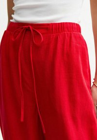 Pantalones de lino rojos con un ajuste relajado, que cuentan con una cinturilla elástica y cierre de cordón. Textura suave, diseño de tiro medio.