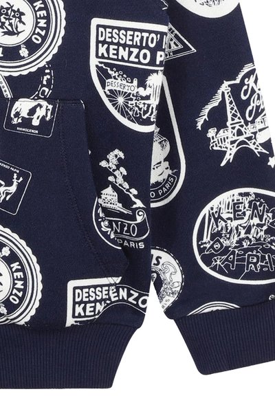 Sweatshirt marine avec des écussons graphiques blancs représentant divers monuments et designs. Tissu en coton, poignets côtelés et poche kangourou.