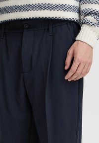 Navy pleated trousers with an elastic waistband, featuring a smooth texture and a side pocket. Match with a patterned knit sweater.