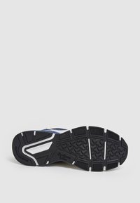 Sneaker med ett marinblått meshinlägg, vita accentfärger och sula av svart gummi med ett texturerat, mönstrat däckdesign. Logotyp synlig.