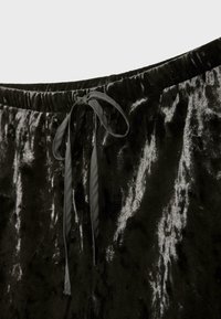 Čierne sametové tepláky s elastickým pásom a predným viazaním. Tkanina má jemný, textúrovaný vzhľad a lesk.