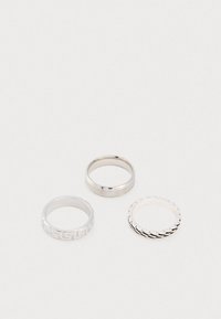 Kolm hõbedast sõrmust: sile bänd, mustriga bänd geomeetrilise disainiga ja keeratud disainiga bänd. Kõik on ümmargused ja metallilised.