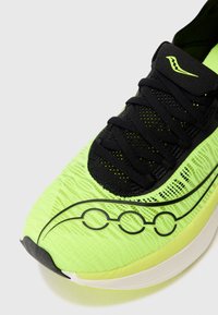 Zapatilla de running verde lima con cordones y detalles en negro; presenta un upper texturizado y un diseño gráfico estilizado a lo largo del costado.