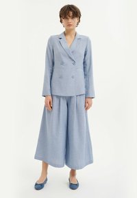 Hellblaues Leinen-Doppelreiher-Blazer mit passenden weiten Hosen. Glatte Textur, zwei vordere Knöpfe und flache Ballerinas.