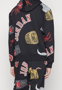 Sudadera con capucha y pantalones negros con gráficos coloridos, incluidos anillos de campeonato dorados y texto "JORDAN", hechos de tela suave con un ajuste cómodo.