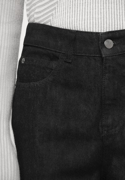 Black denim jeans featuring a classic design with five pockets, a metal button closure, and a smooth texture. Partially visible white striped fabric above.