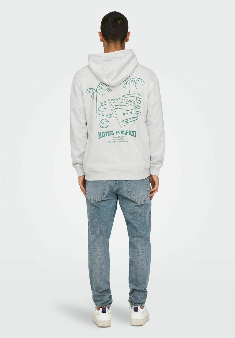 Sweat à capuche gris en mélange de coton, avec un imprimé graphique vert représentant des palmiers et du texte au dos. Associé avec un jean bleu clair et des baskets.