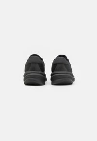 Black athletic shoes featuring a textured mesh upper, padded collar, and a thick rubber sole. Design includes a subtle logo detail on the heel.