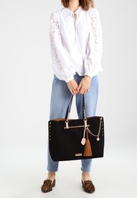 Grand sac fourre-tout en suède noir avec une anse en chaîne, des accents roses et un gland. Remarquable pour ses détails cloutés sur les côtés et son haut arrondi.