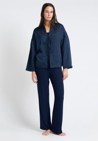 Granatowy zestaw odzieży do relaksu z fakturowaną, wzorzystą kurtką z zapięciem na sznur i szerokimi rękawami, w połączeniu z dopasowanymi, luźnymi spodniami.