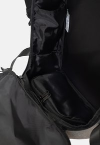 Interno di una borsa nera in tessuto con più scomparti, tra cui una sezione con zip, texture liscia e design minimalista.