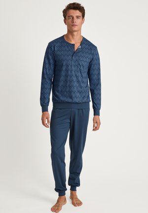 Marineblauw loungewear-set met een langemouwen top met een geometrisch patroon en een stolpplooi, aangevuld met bijpassende taps toelopende broek.