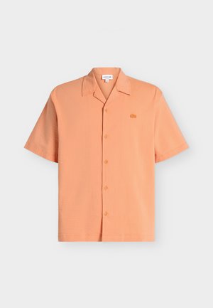 Chemise à manches courtes boutonnée en orange clair avec un petit logo crocodile brodé sur la poitrine gauche, présentée sur fond blanc.