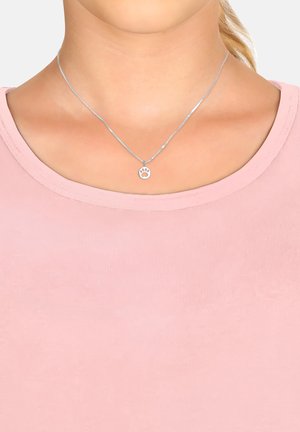 Silver necklace with a small circular paw print pendant, worn over a light pink rounded neckline top, showcasing a smooth texture.