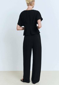 Černý peplum top s krátkými rukávy, doplněný o široké kalhoty v odpovídající barvě. Vyrobený z texturované tkaniny, s jemným detailem zadního zipu.
