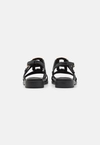 Black leather sandals with a flat sole, open back design, and multiple cross straps providing ventilation. Gold-tone hardware accents visible.