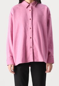Pink, button-up shirt made of soft wool blend with a collared neck and long sleeves; features a relaxed fit and textured fabric.