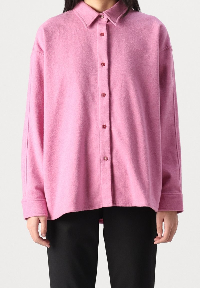 Pink, button-up shirt made of soft wool blend with a collared neck and long sleeves; features a relaxed fit and textured fabric.