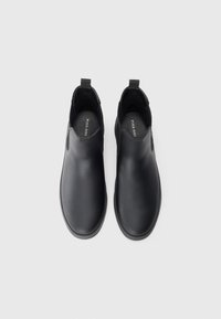 Zapatos negros de cuero tipo slip-on con paneles elásticos a los lados, punta redondeada, parte superior texturizada y tirador para facilitar su uso. Suela plana de goma.