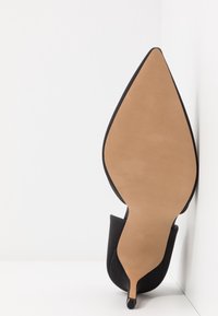 Scarpa con tacco a stiletto nero e punta affilata. La tomaia in pelle liscia si fonde con una suola beige. Presenta un design con ritagli ai lati.