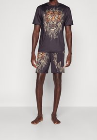 Man som står barfota och bär matchande mörka träningsshorts och t-shirt med en aggressiv orange tiger-grafik.