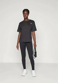 Fekete, rövid ujjú póló diszkrét logóval, fekete leggingsszel és fehér sneakers-szel párosítva, letisztult, sportos szabásban.