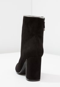 Black suede ankle boot with a chunky heel, silver trim at the top edge, and a side zipper. Smooth texture with a matte finish.