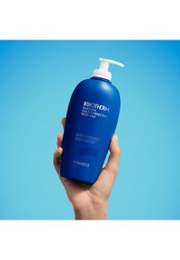 Blå plastflaske med Biotherm Biocorps Multi-Corrective Body Milk. Rund form, pumpe-dispenser på toppen, 400 ml volum, minimal tekst.