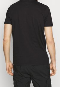 Camiseta de algodón negra de manga corta, diseño minimalista y cuello redondo. Textura suave, extremos de la cola ligeramente curvados. Detalles de costura claros.