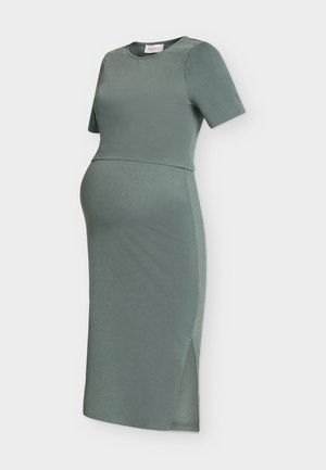 Moosgrünes Umstandskleid mit kurzen Ärmeln, rundem Ausschnitt, figurbetonter Silhouette und seitlichem Schlitz vor einfarbigem Hintergrund.