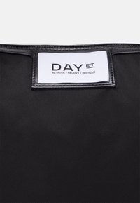 Schwarze, strukturierte Tragetasche mit einem weißen Etikett, auf dem "DAY ET" und "RETHINK - RELOVE - RECYCLE" steht. Verfügt über einen Reißverschluss und verstärkte Kanten.