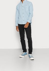 Camisa de manga larga a rayas azul claro y blanca con diseño de botón, combinada con jeans ajustados negros y zapatillas deportivas azules.
