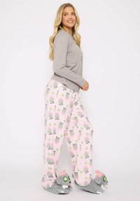 Gray long-sleeve top with a rounded neckline paired with pink pajama pants featuring a repeated cartoon animal pattern. Gray slippers with animal design.