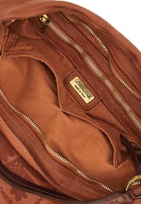 Interno di una borsa a tracolla in pelle marrone con diversi scomparti con zip, una fodera in tessuto e un'etichetta metallica con il nome del marchio.